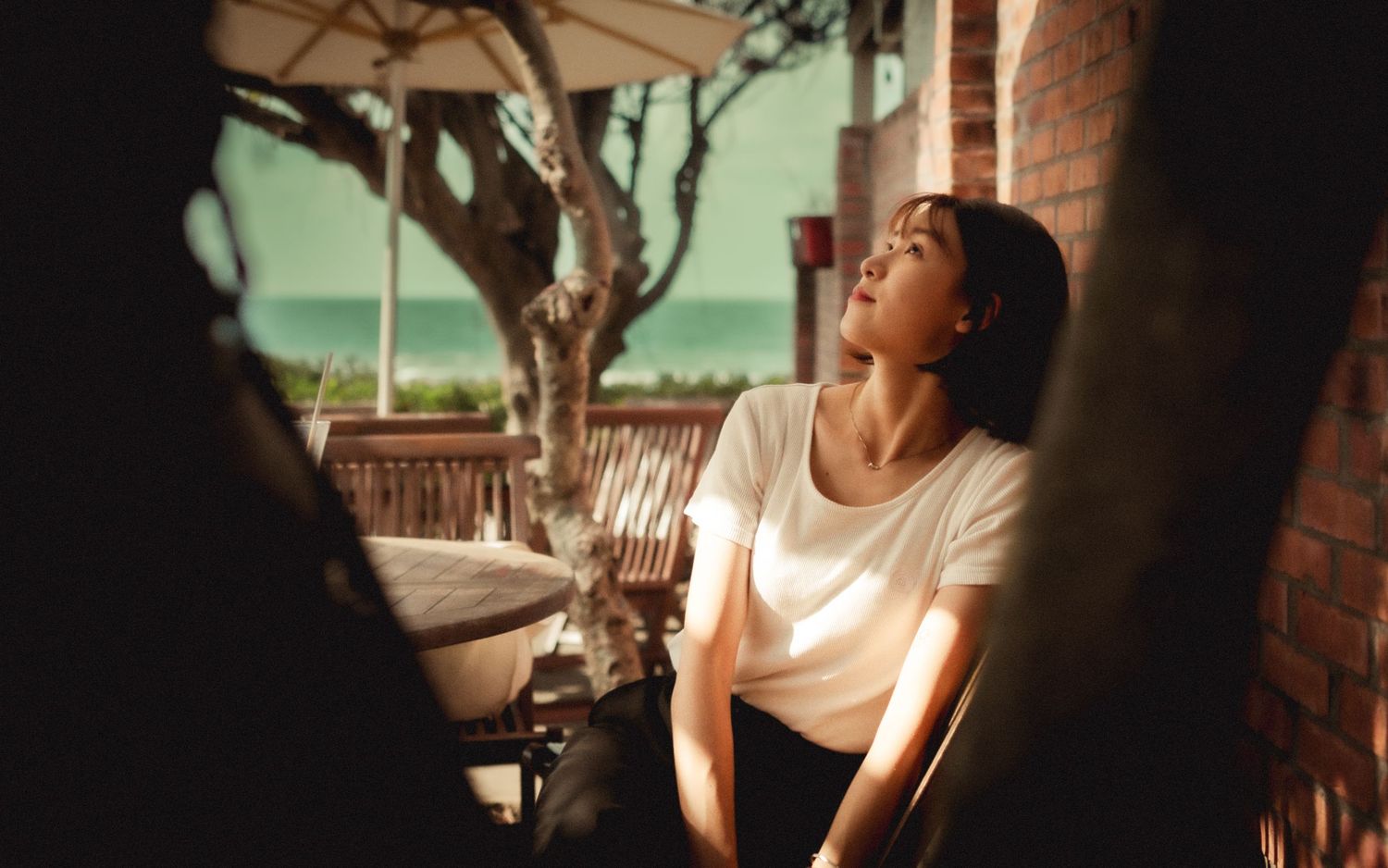 Person in white shirt relaxing outdoors on a porch with natural lighting.