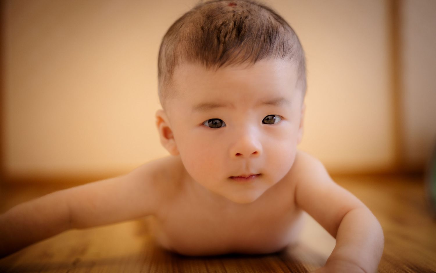 Close up of baby lying on wooden floor with gentle lighting.