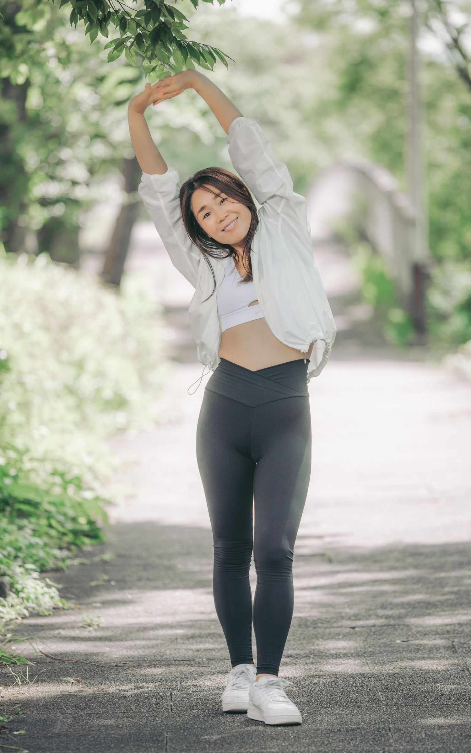 Person in athletic wear stretching outdoors on tree-lined path in soft natural lighting.