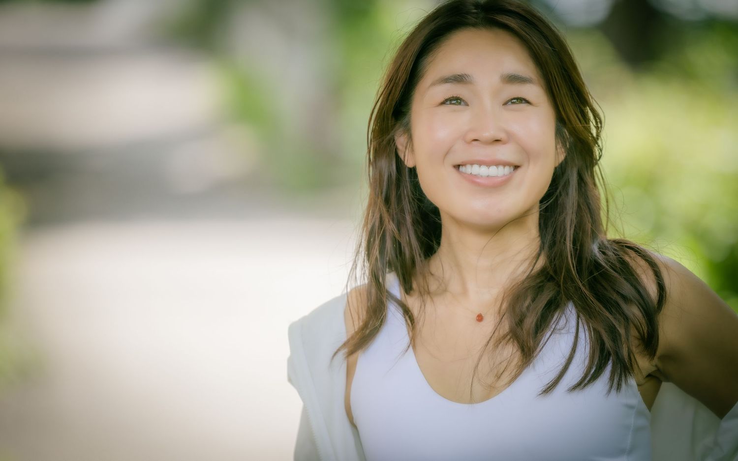 Person in white tank top smiling outdoors with natural lighting.