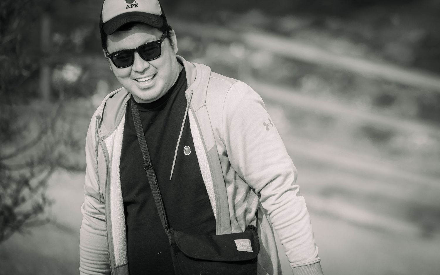 Person in casual wear and baseball cap with sunglasses in black and white portrait.