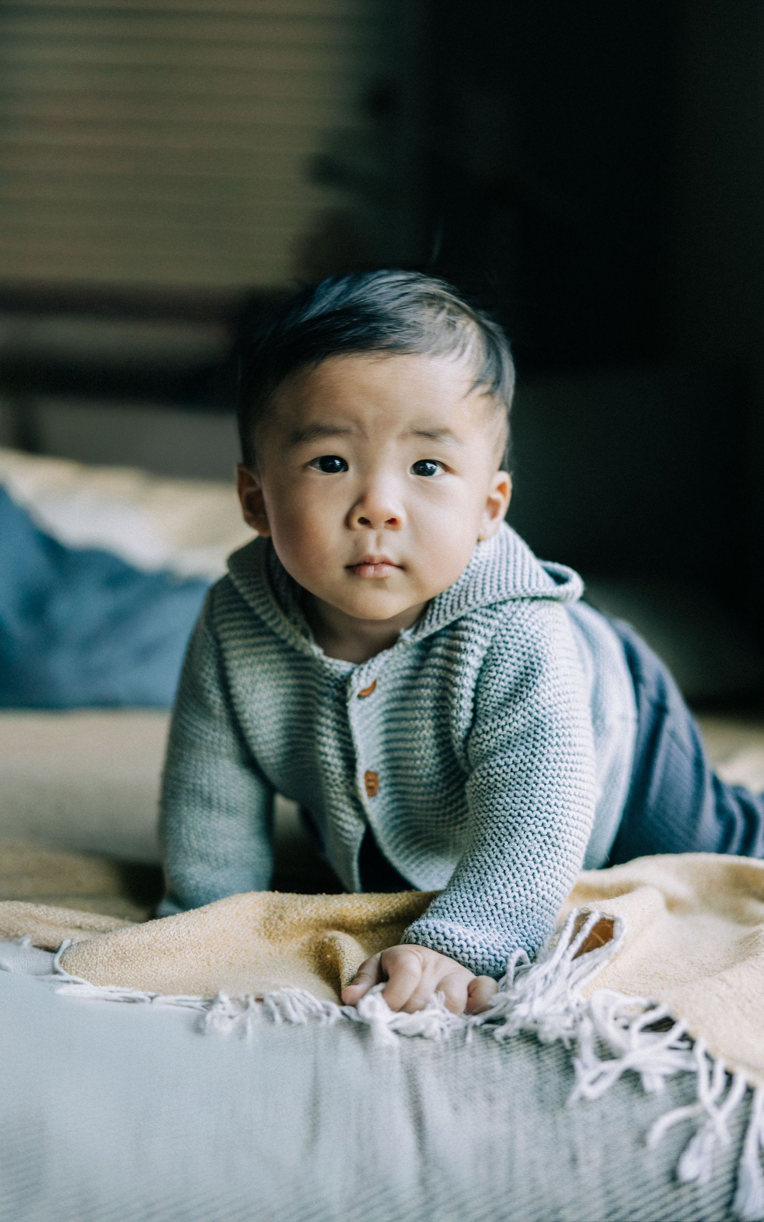 Baby in hooded gray sweater lying on light colored blanket.