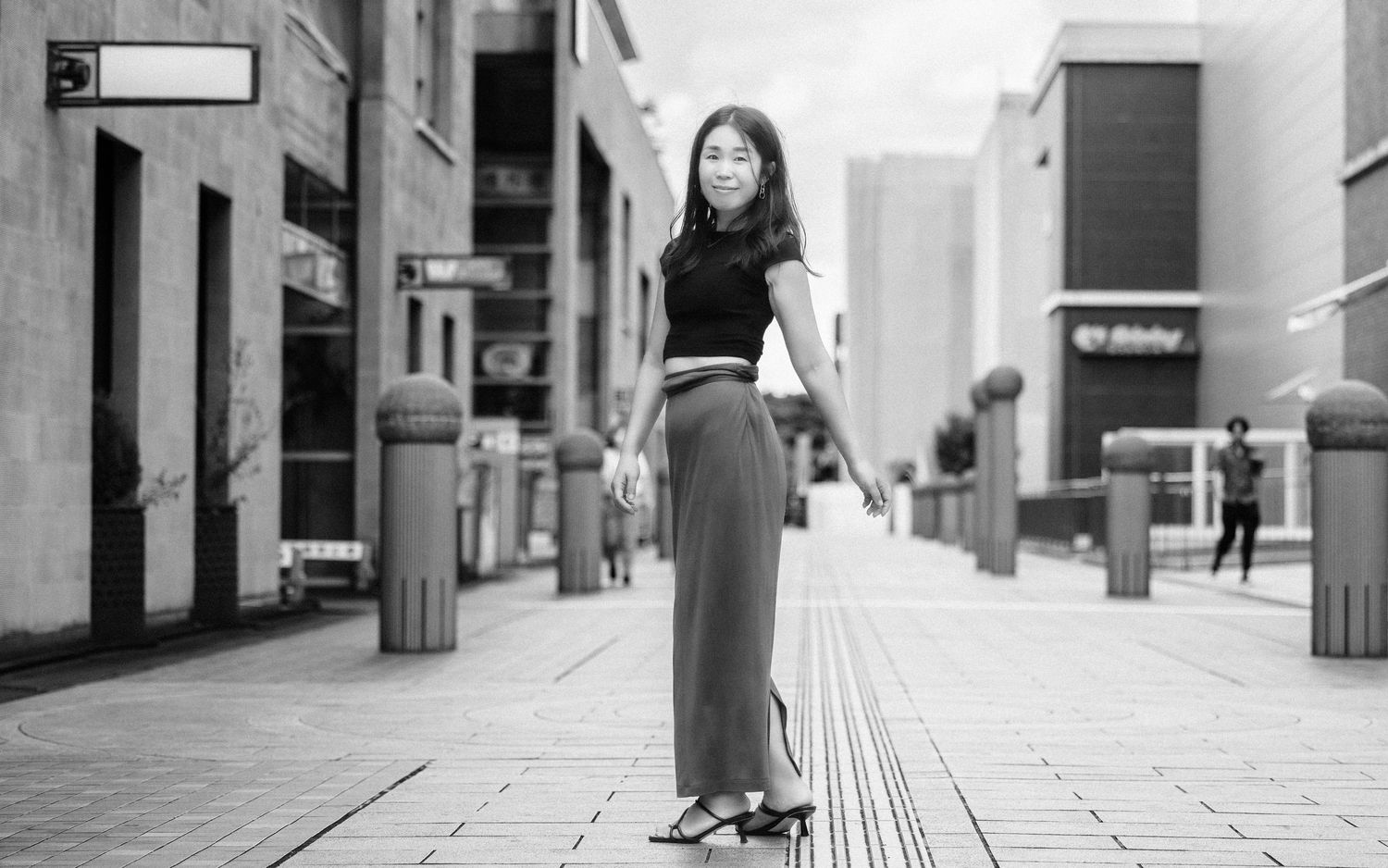 Person in black crop top and wide-leg pants posing on urban street in black and white.