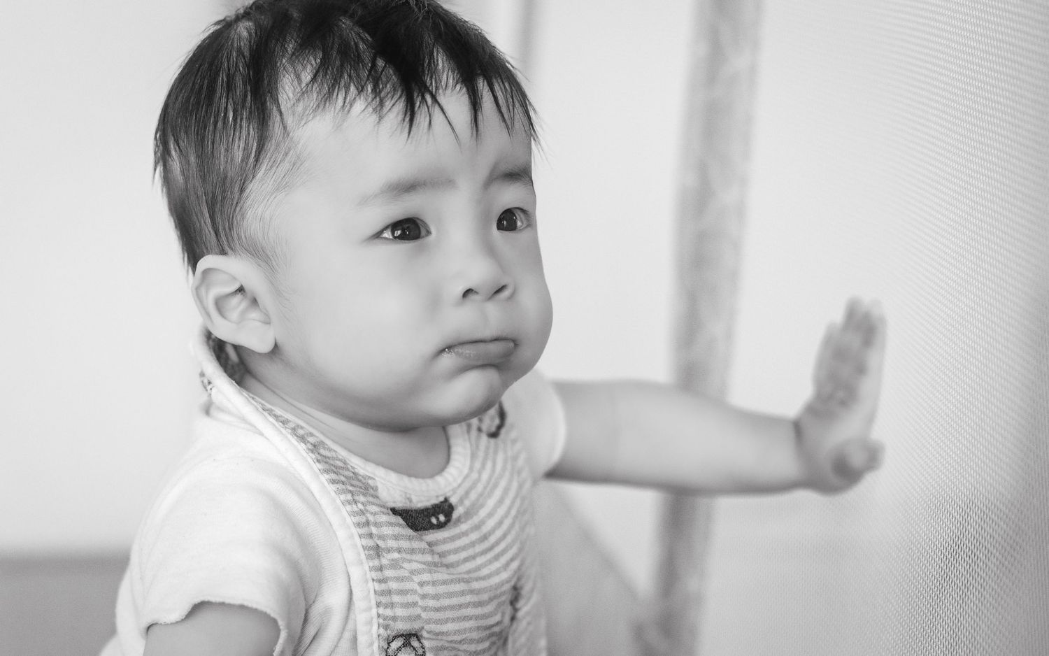 Black and white portrait of toddler in striped shirt looking to the side with a curious expression.