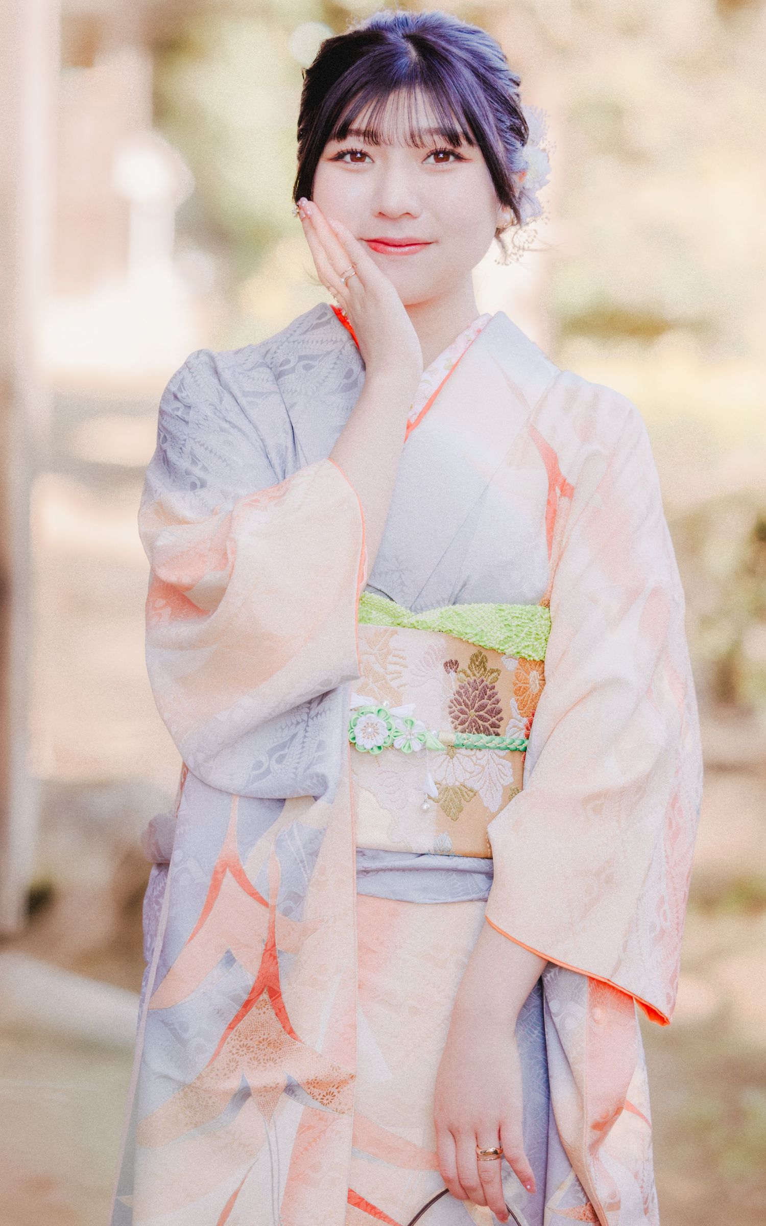 Person in delicate peach and grey kimono with floral obi sash poses in garden setting.
