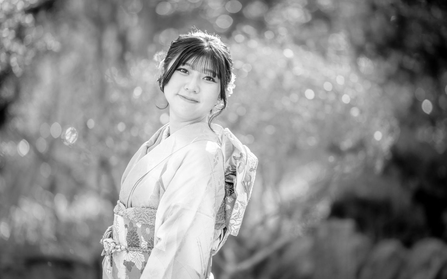 Person in traditional Japanese kimono stands gracefully in soft focus garden setting.