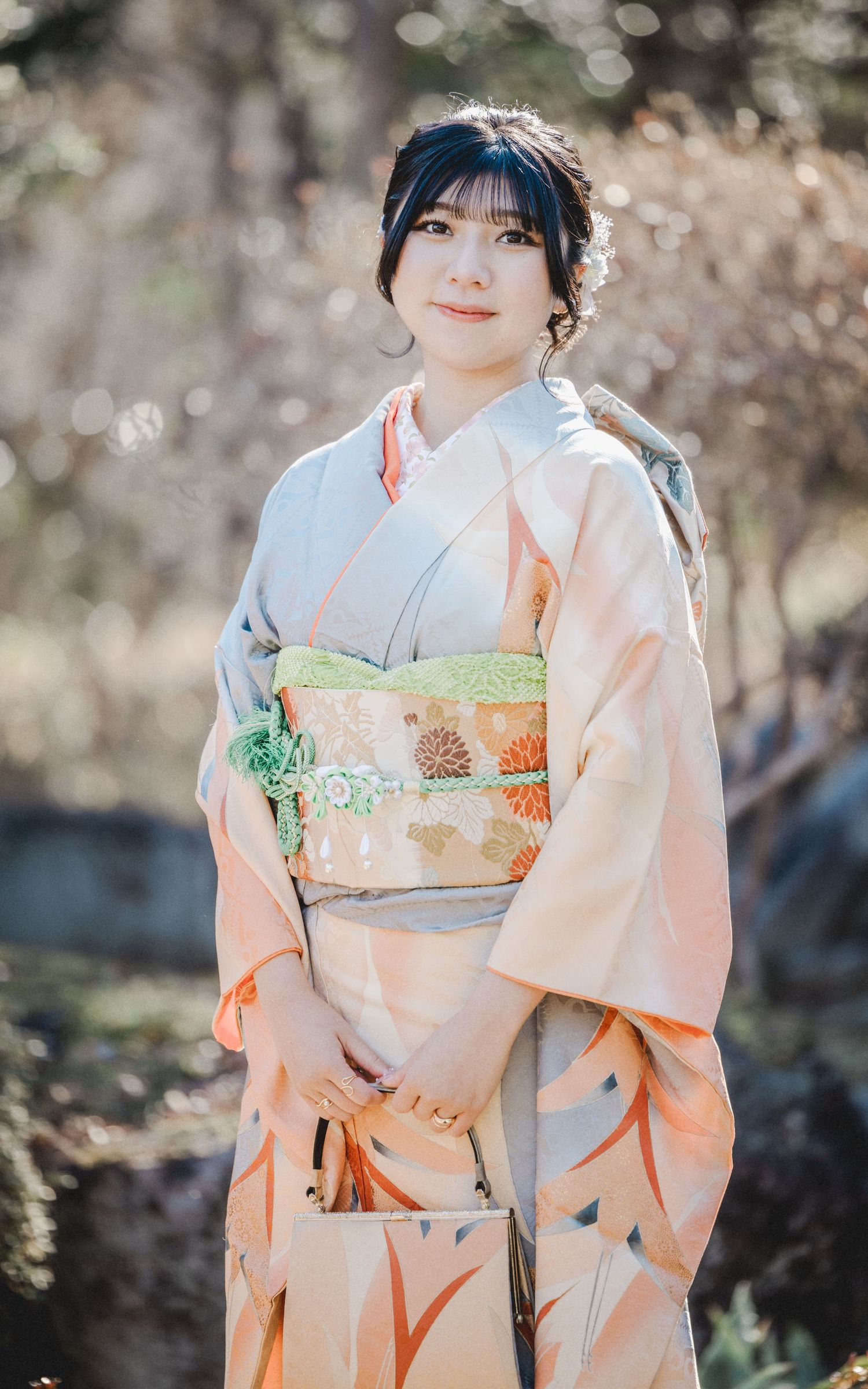 Person wearing peach kimono with mint green obi poses in sunlit garden setting.