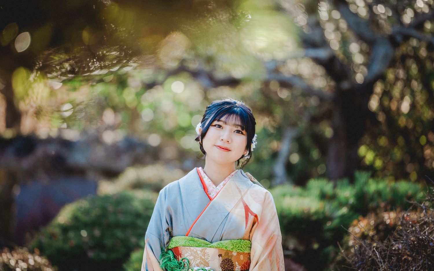 A serene garden scene with a person wearing a pale kimono with orange accents against natural foliage.