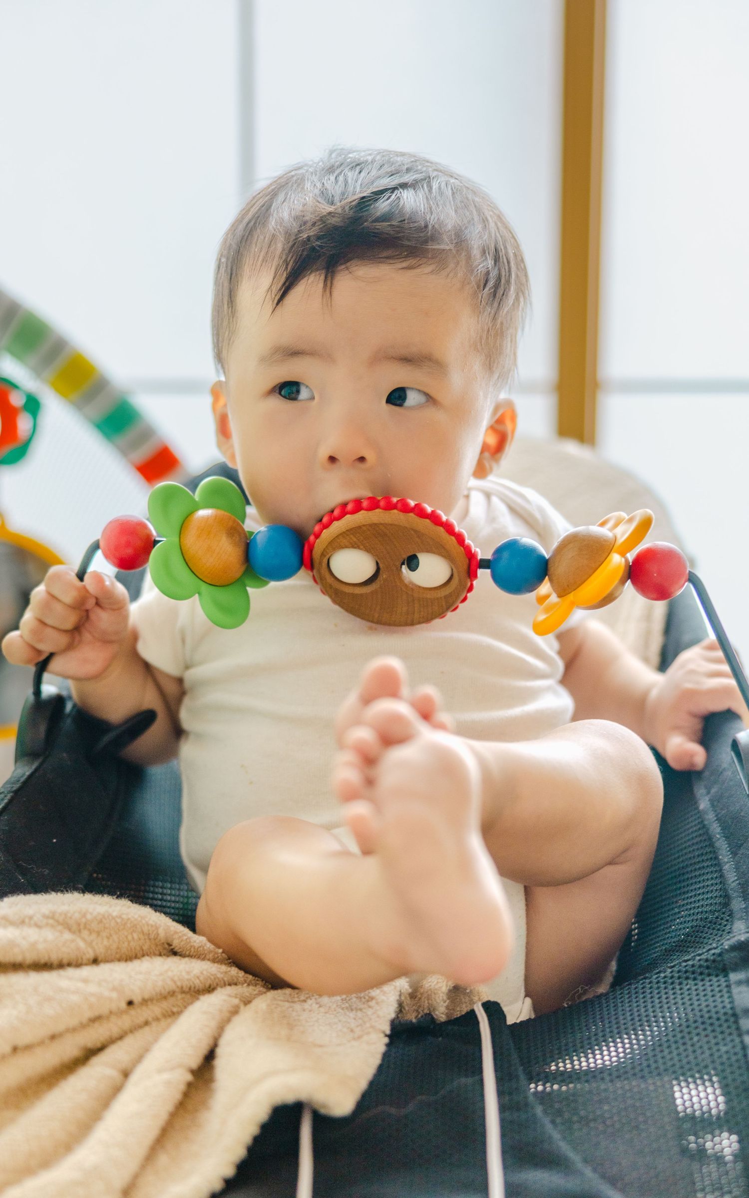 Baby sitting with colorful toy beads and wearing white onesie.