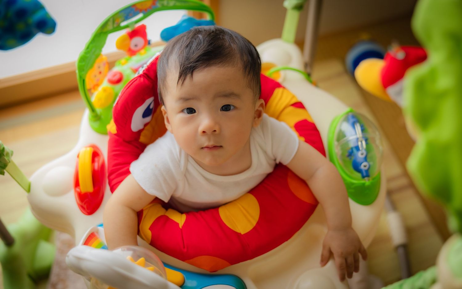 Baby in white outfit playing on colorful cushioned play mat with toys.