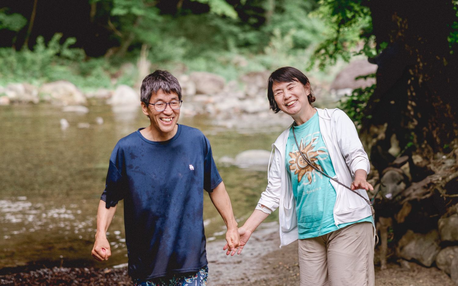 Two people walking together by a stream in a forest setting.