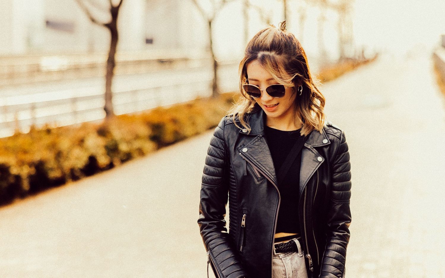 Person wearing black leather jacket and sunglasses stands confidently on outdoor path.