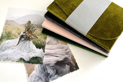 A wedding photo lies beside green velvet-bound photo albums or books on a white surface.