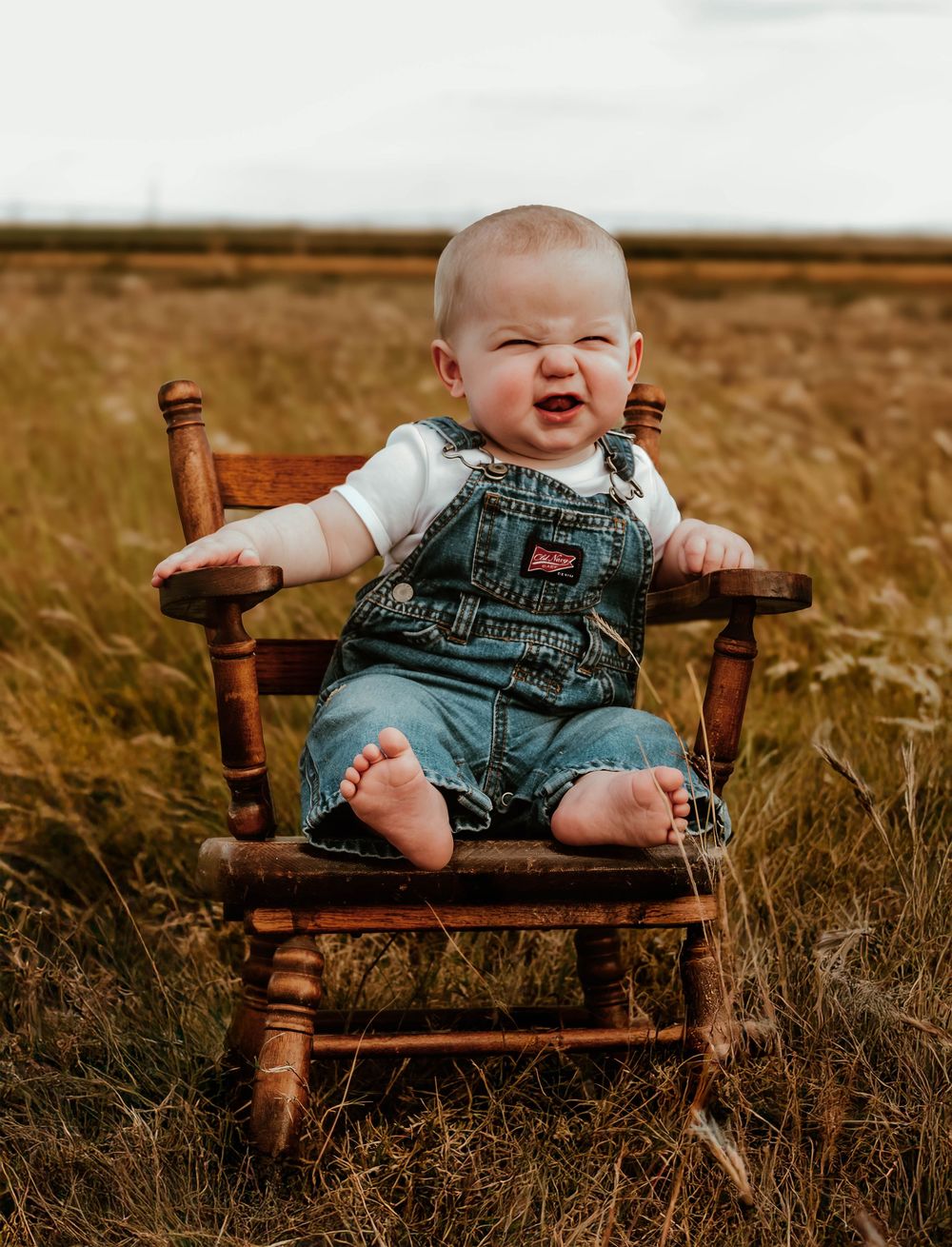 Series showing a baby in denim overalls sitting and laughing on a wooden bench in a field.