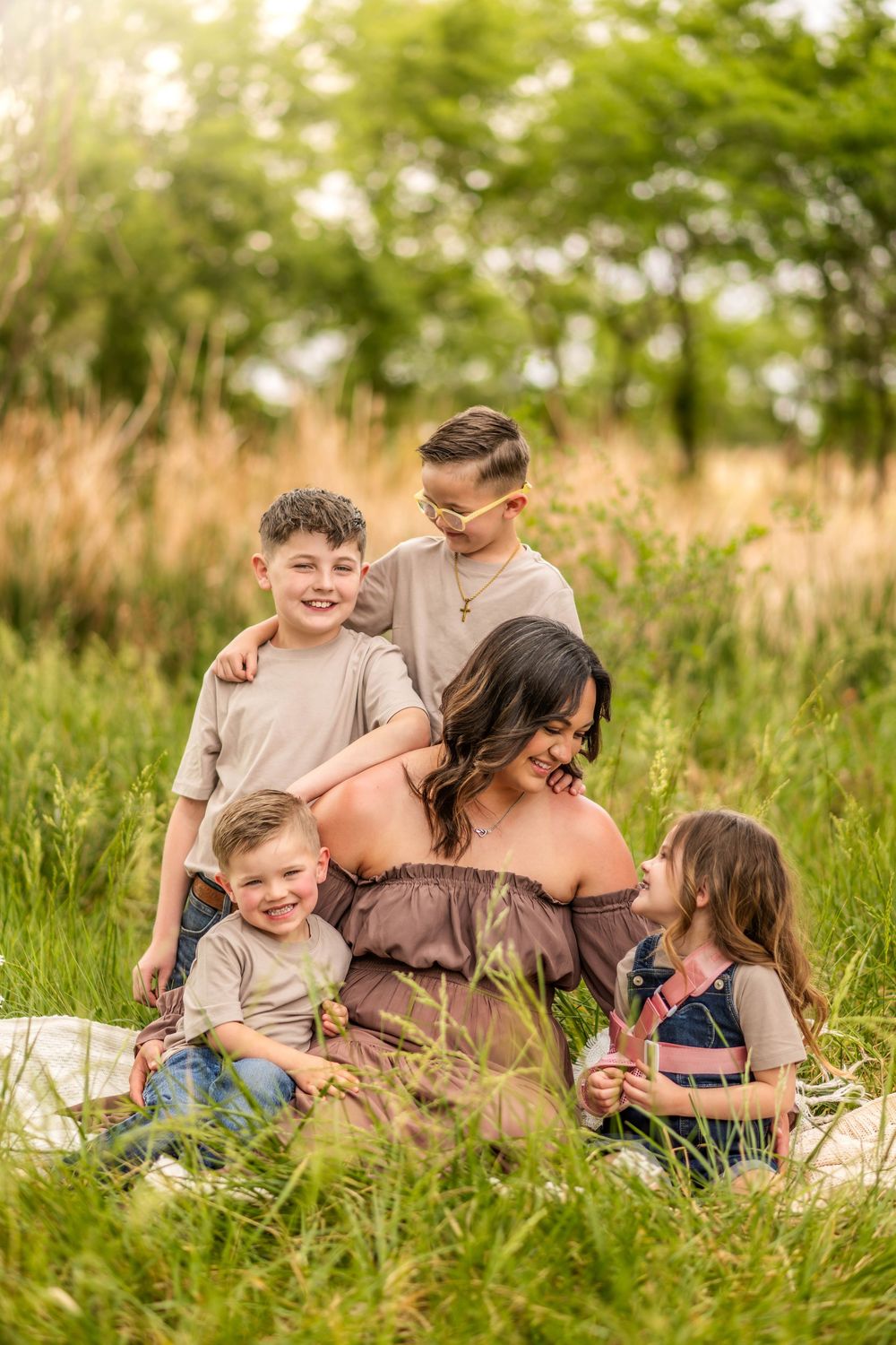 Pregnant woman sitting in a green meadow surrounded by her four happy children during an outdoor maternity photo session.
