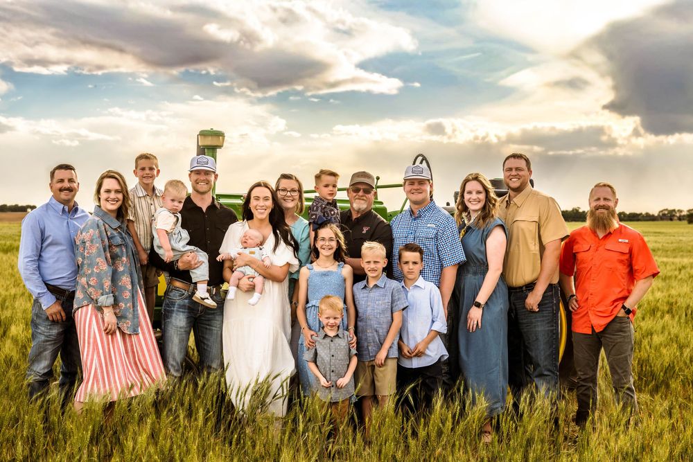 Large family group portrait in a green field with dramatic sky, wearing casual and denim outfits.