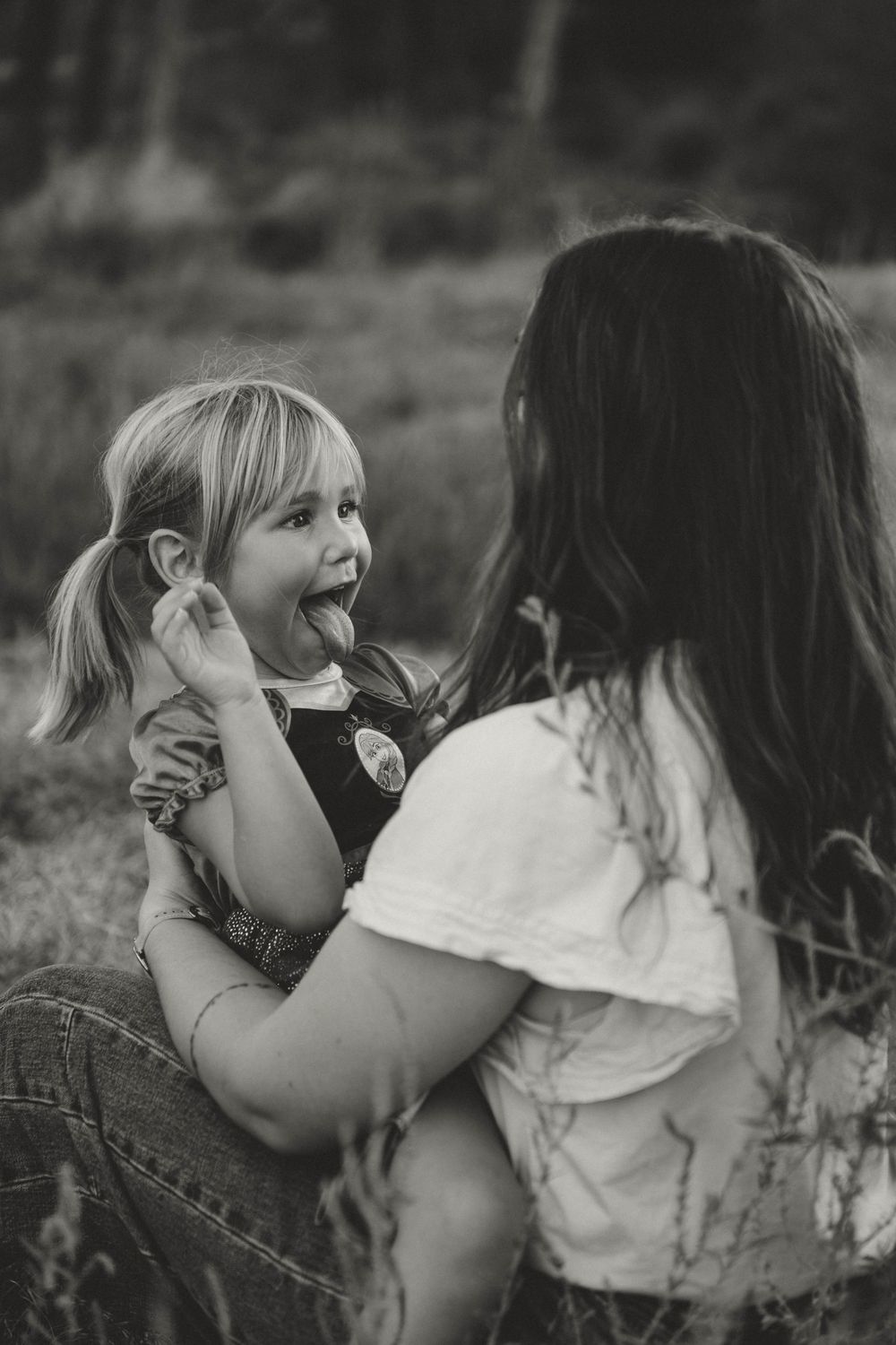 Black and white photo of a laughing little girl being held by a woman outdoors in a field.