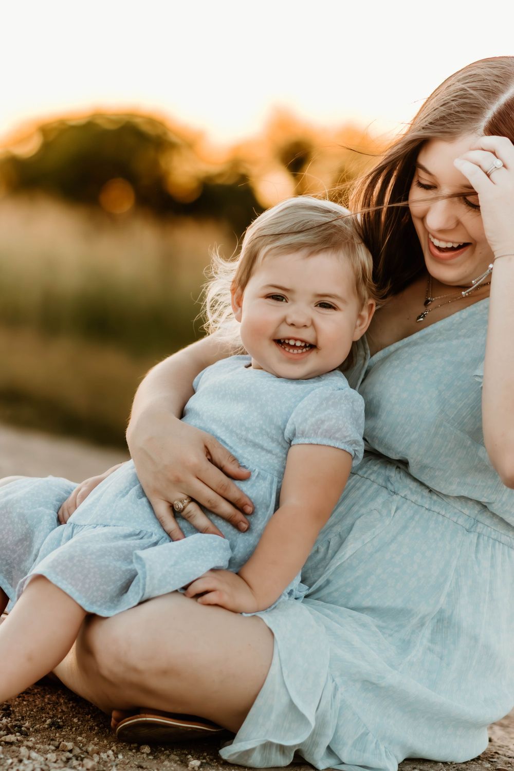 Mother and child in blue dresses sharing joyful moment during golden hour.