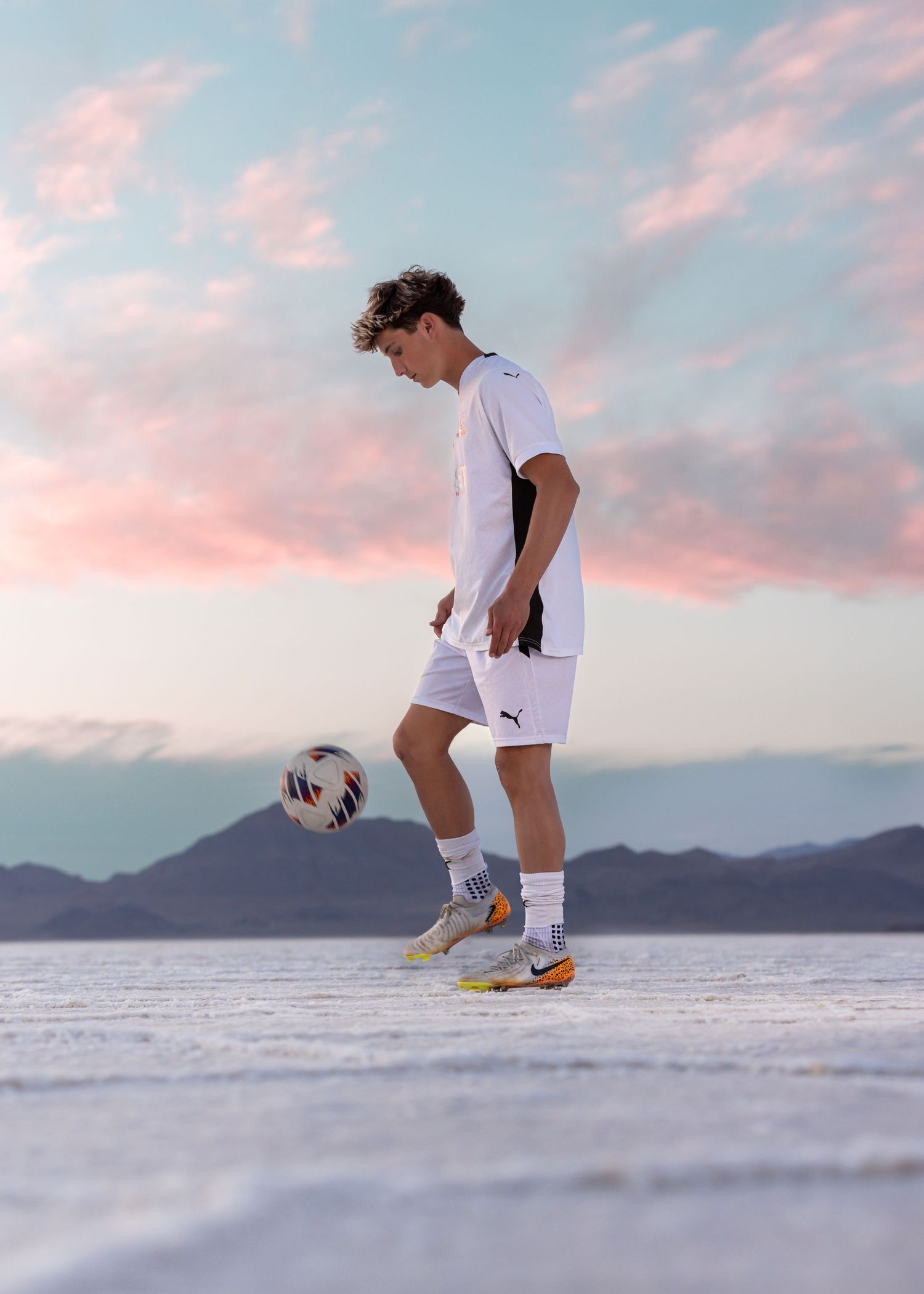 Utah Senior Soccer player poses for Bonneville Salt Flats Photography in all practicing freestyle at sunset against mountain backdrop.