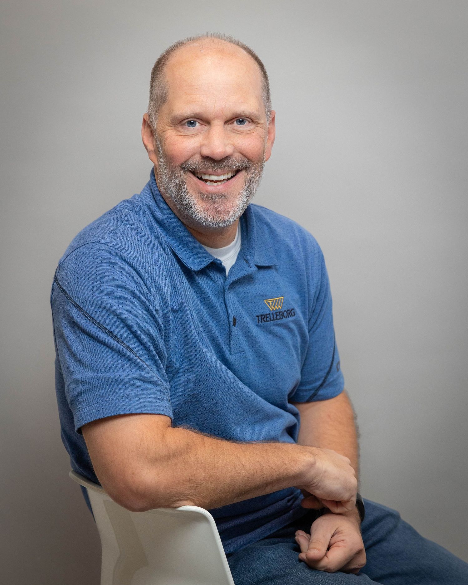 Smiling middle-aged man in blue polo shirt seated casually for a professional headshot photo.