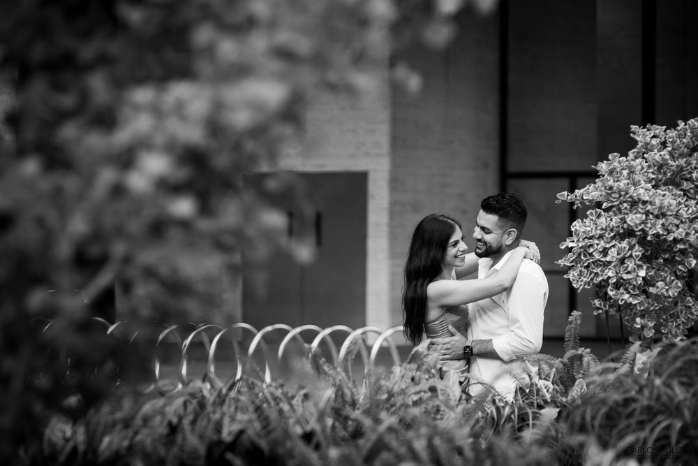 Black and white portrait of couple sharing tender moment among garden foliage.