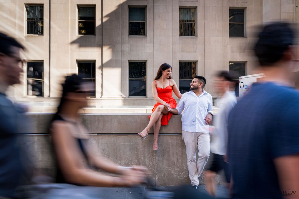 Couple in red and white outfits amid blurred city pedestrians by stone building.