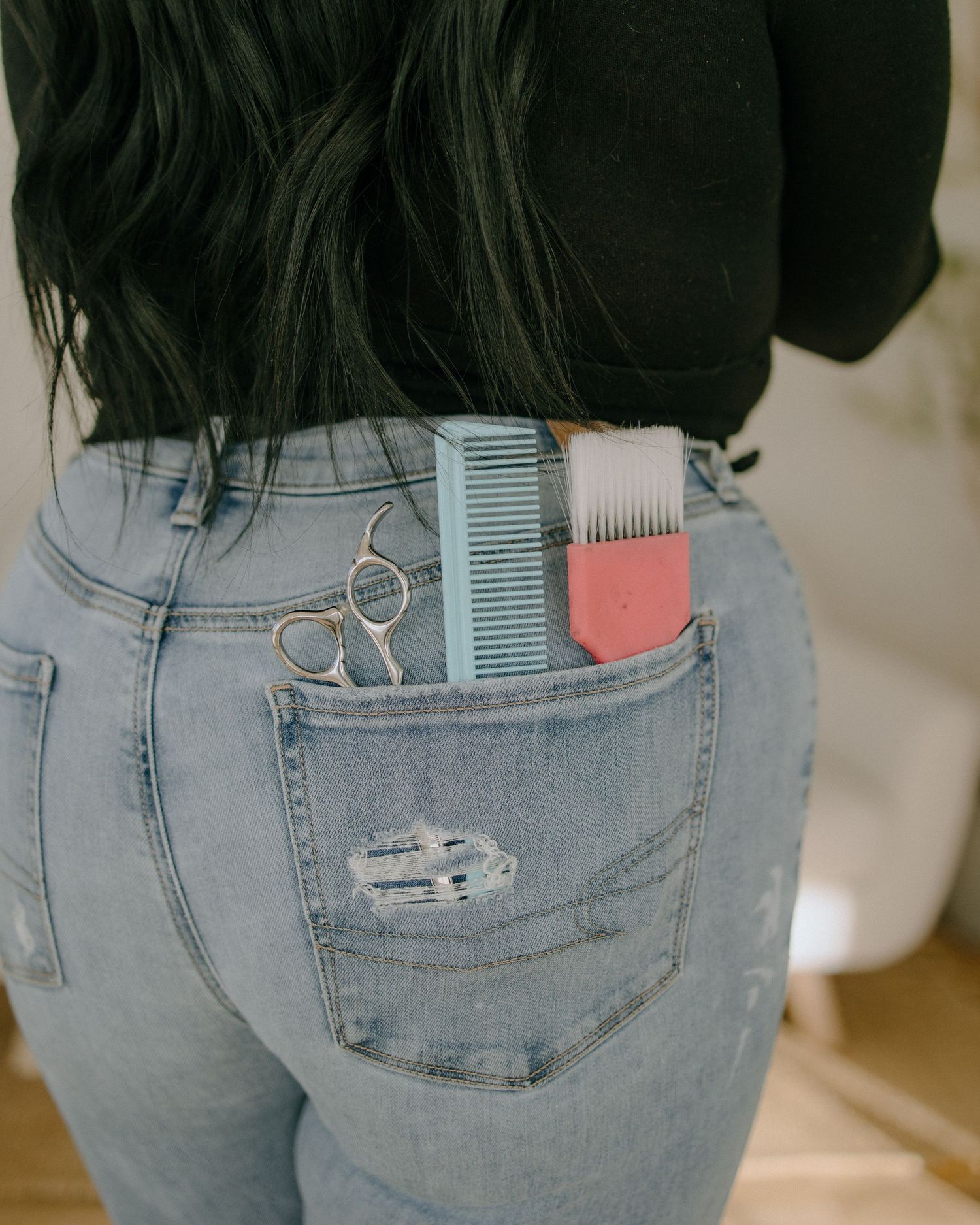 Close-up of hair styling tools tucked into back pocket of distressed blue jeans.