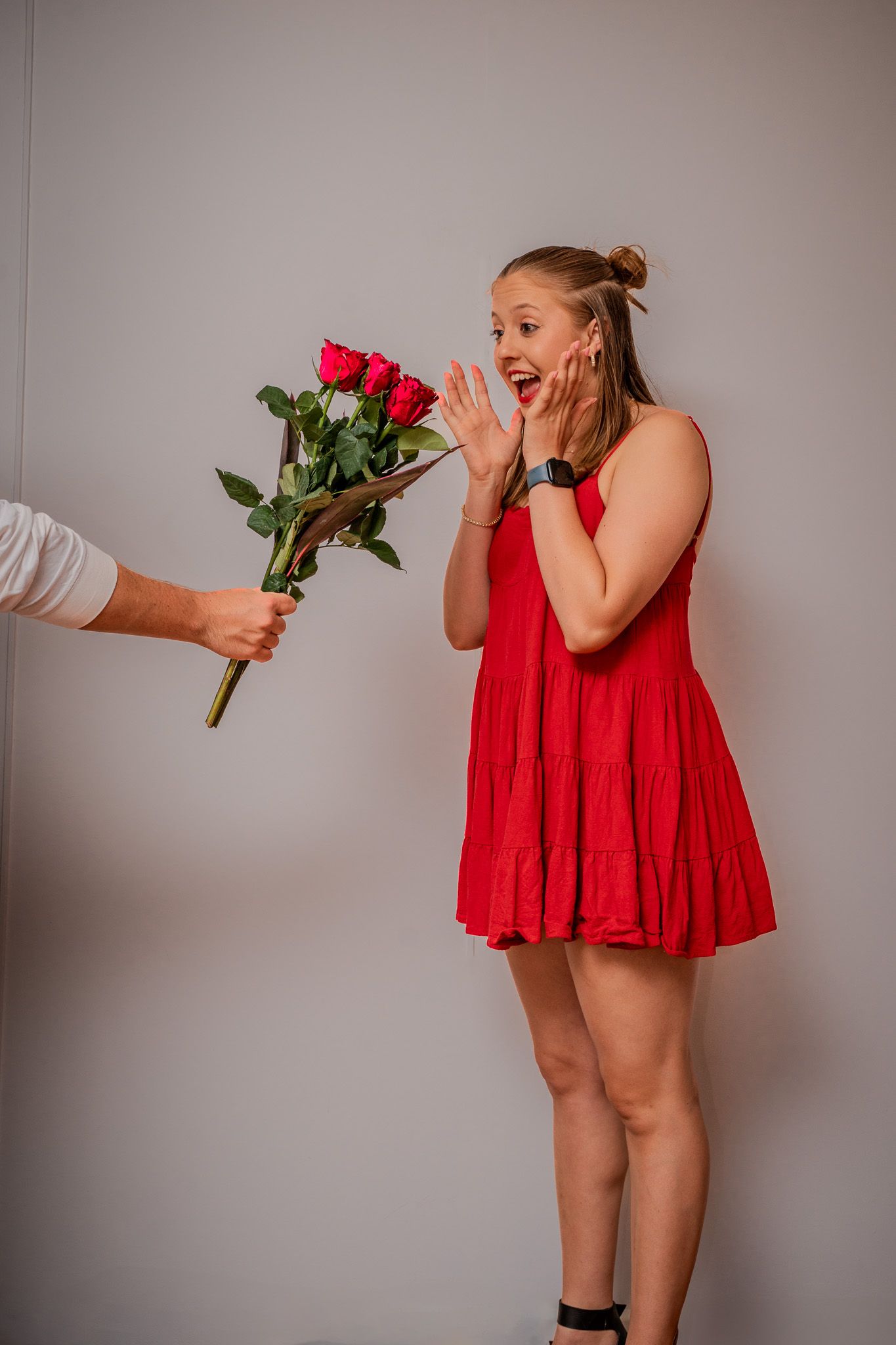 Someone in a red dress reacts with surprise as they receive a bouquet of red roses.