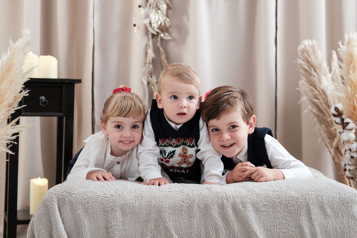 Row of children posing playfully on floor with holiday decorations visible behind them.
