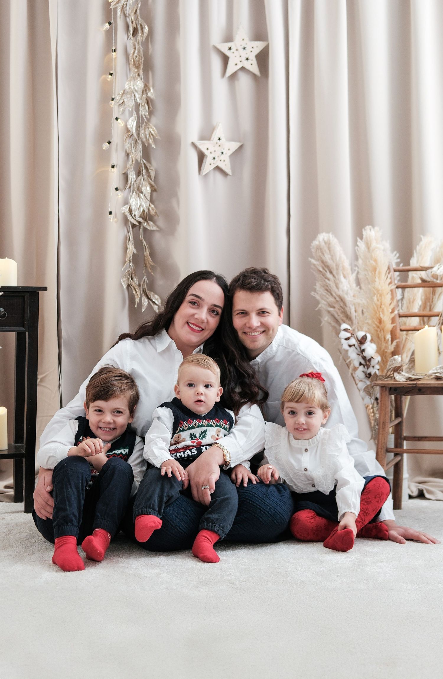 Family wearing white and black holiday outfits lying together on floor with festive star decorations.