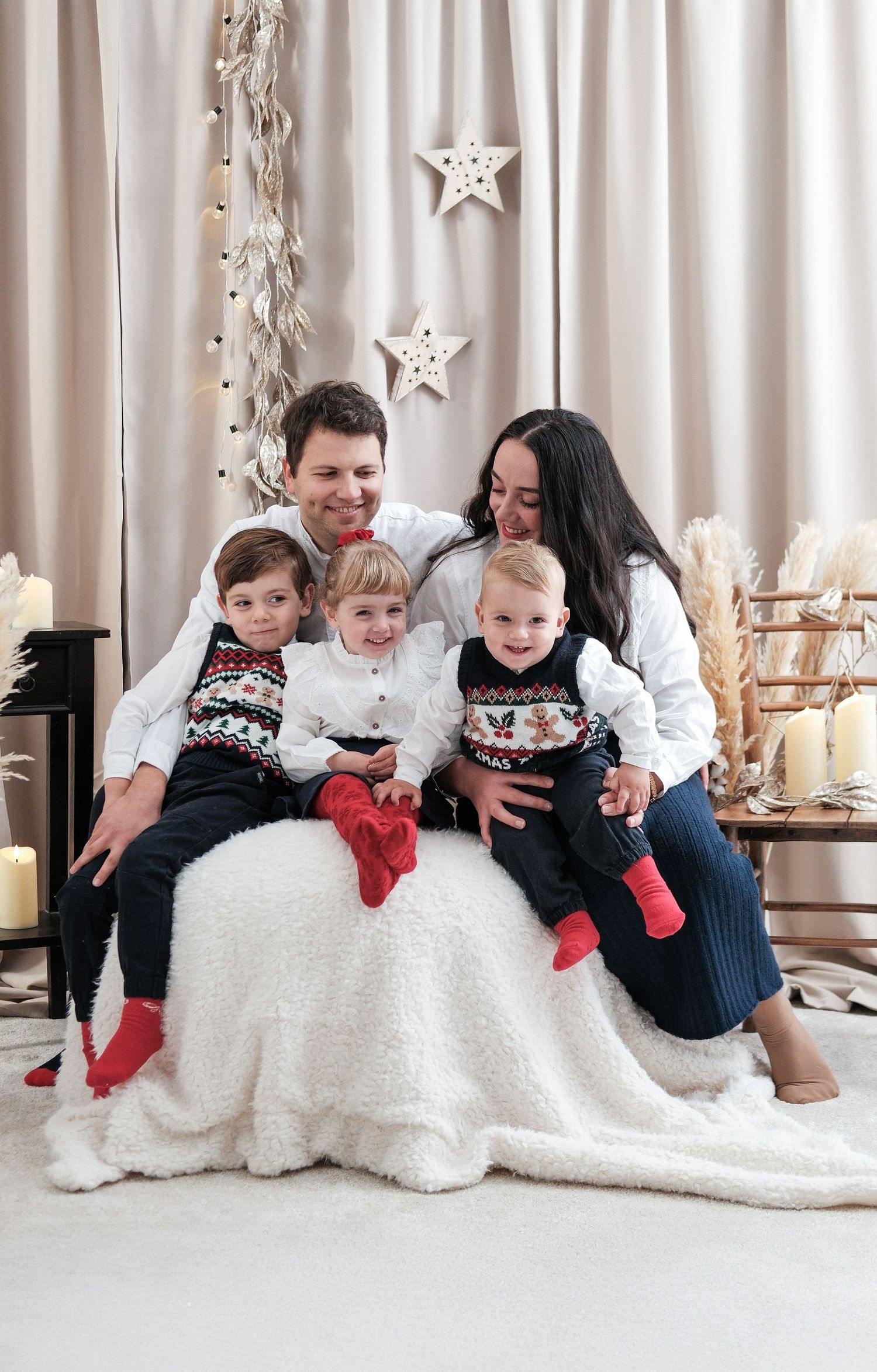 Holiday family photo with group lounging on white blanket wearing coordinated winter outfits.