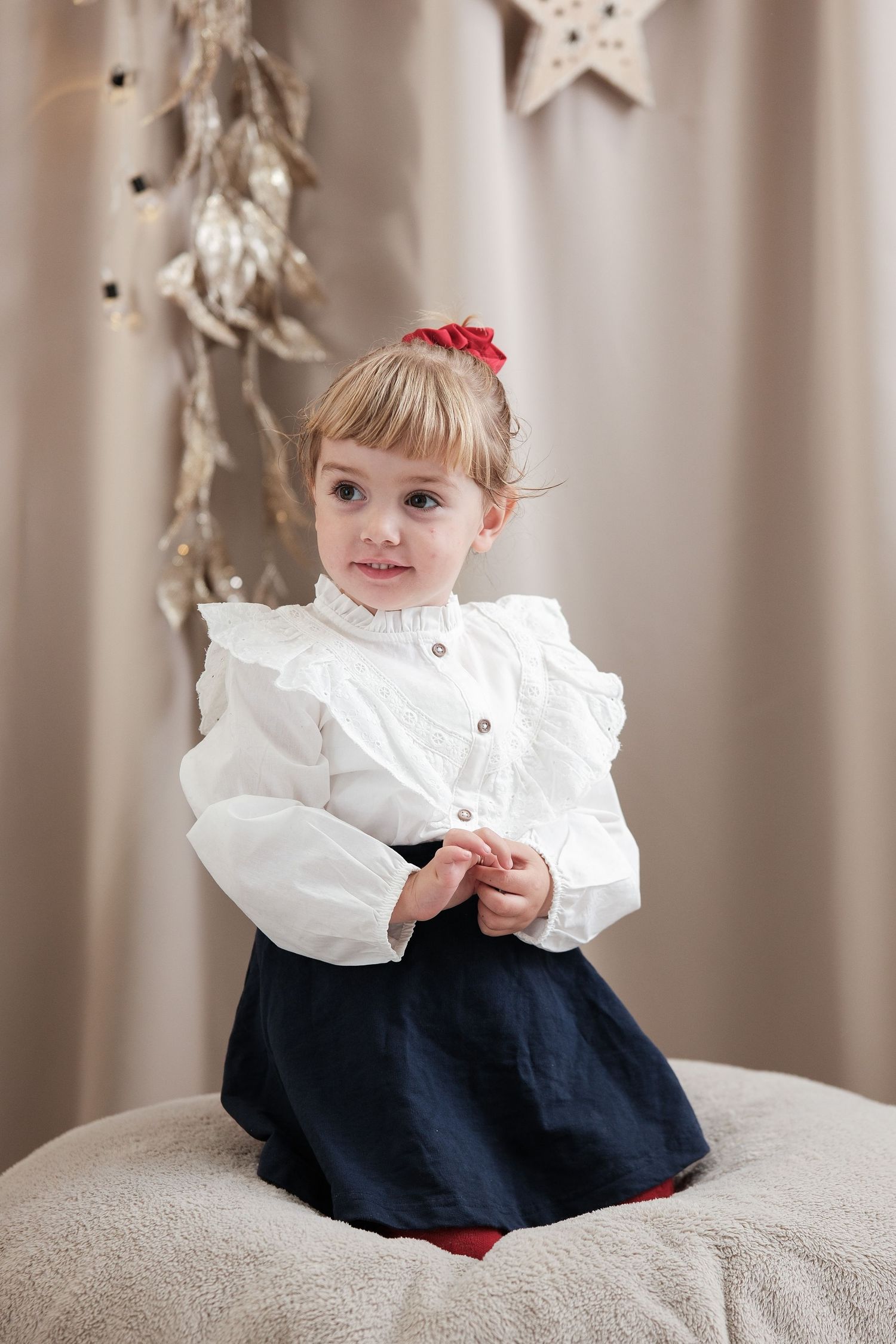 Child in white ruffled top and navy dress sitting on gray couch with star decorations.