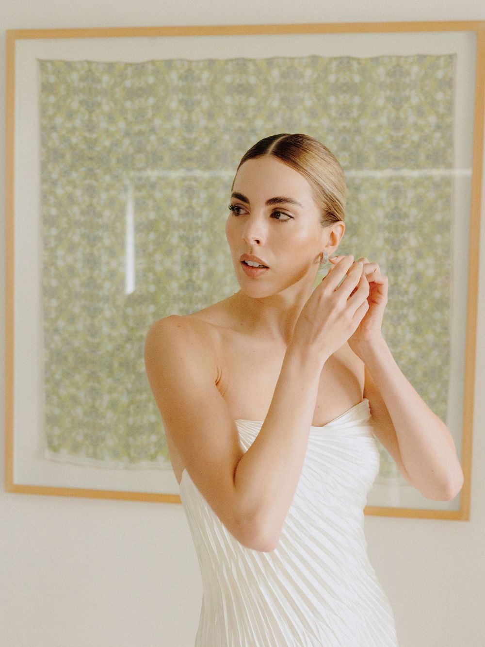 Elegant bridal portrait showing delicate pleated white gown against sage green wallpaper.