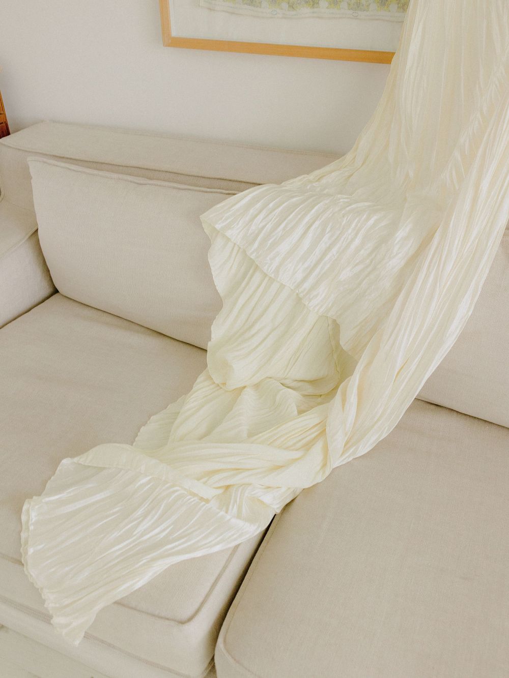 A flowing white wedding gown draped elegantly across a cream-colored couch.