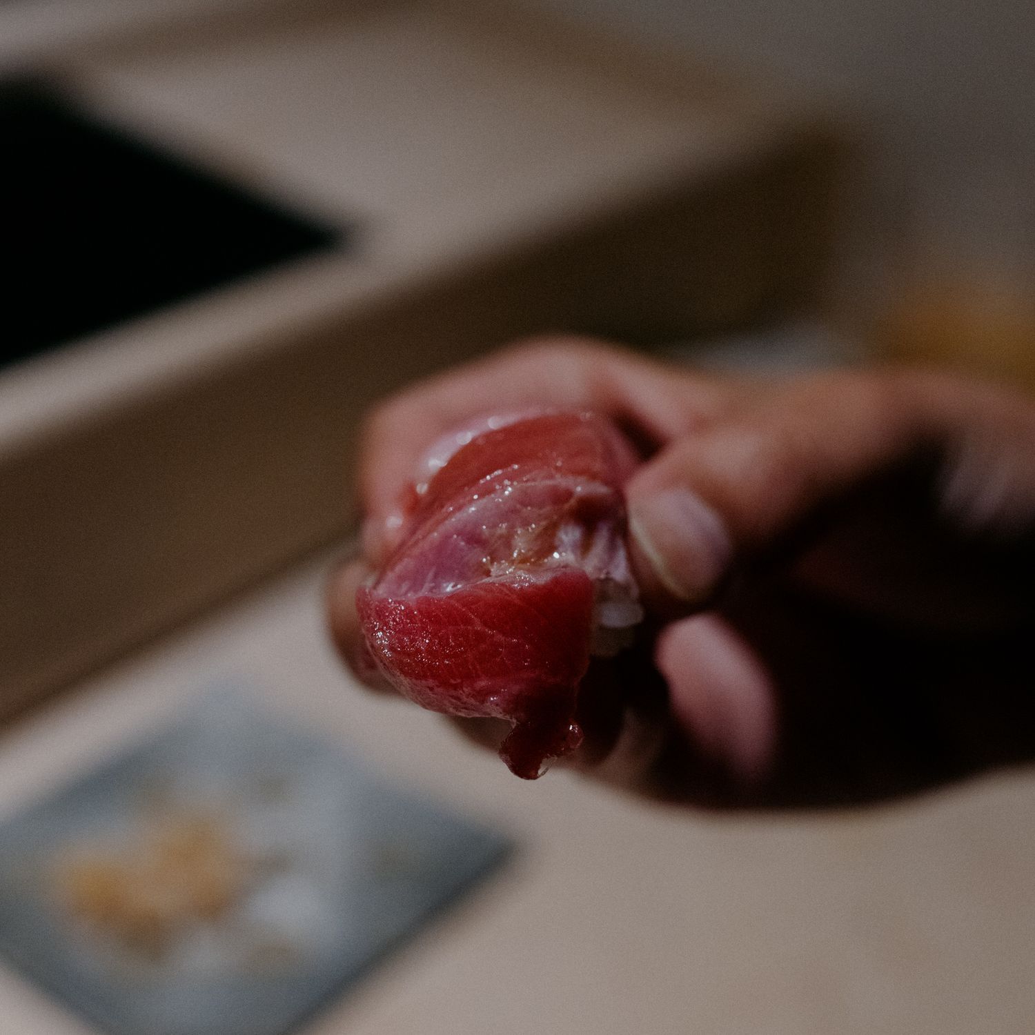 Fingers holding a glistening piece of red tuna sashimi.