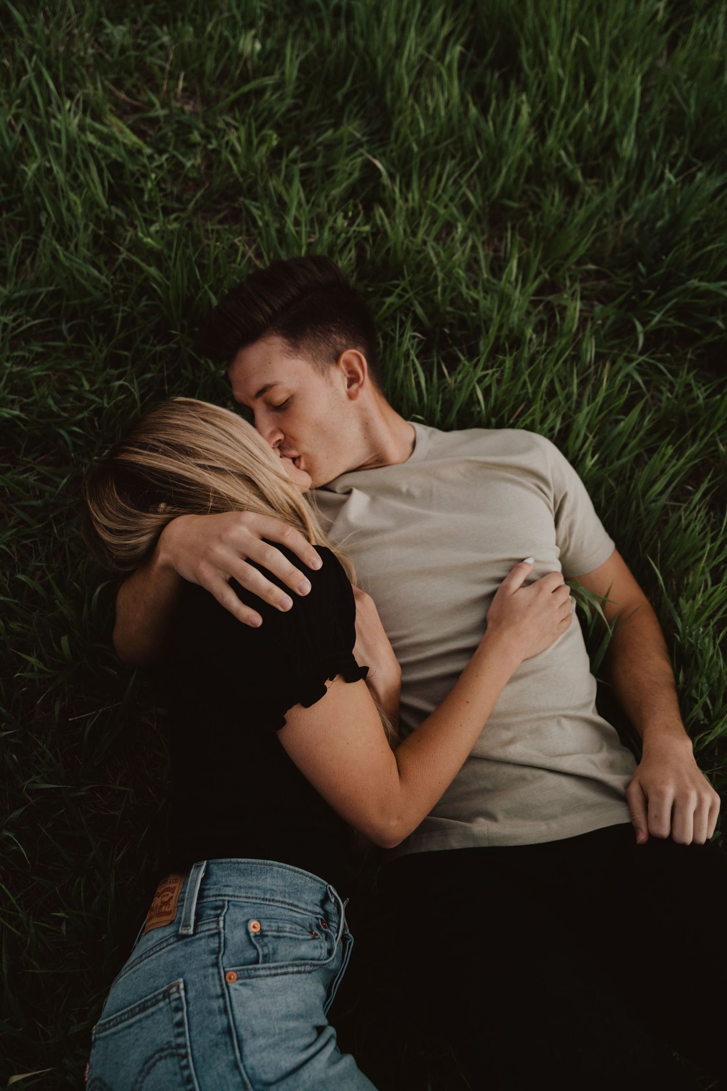 Couple lying together intimately on green grass.