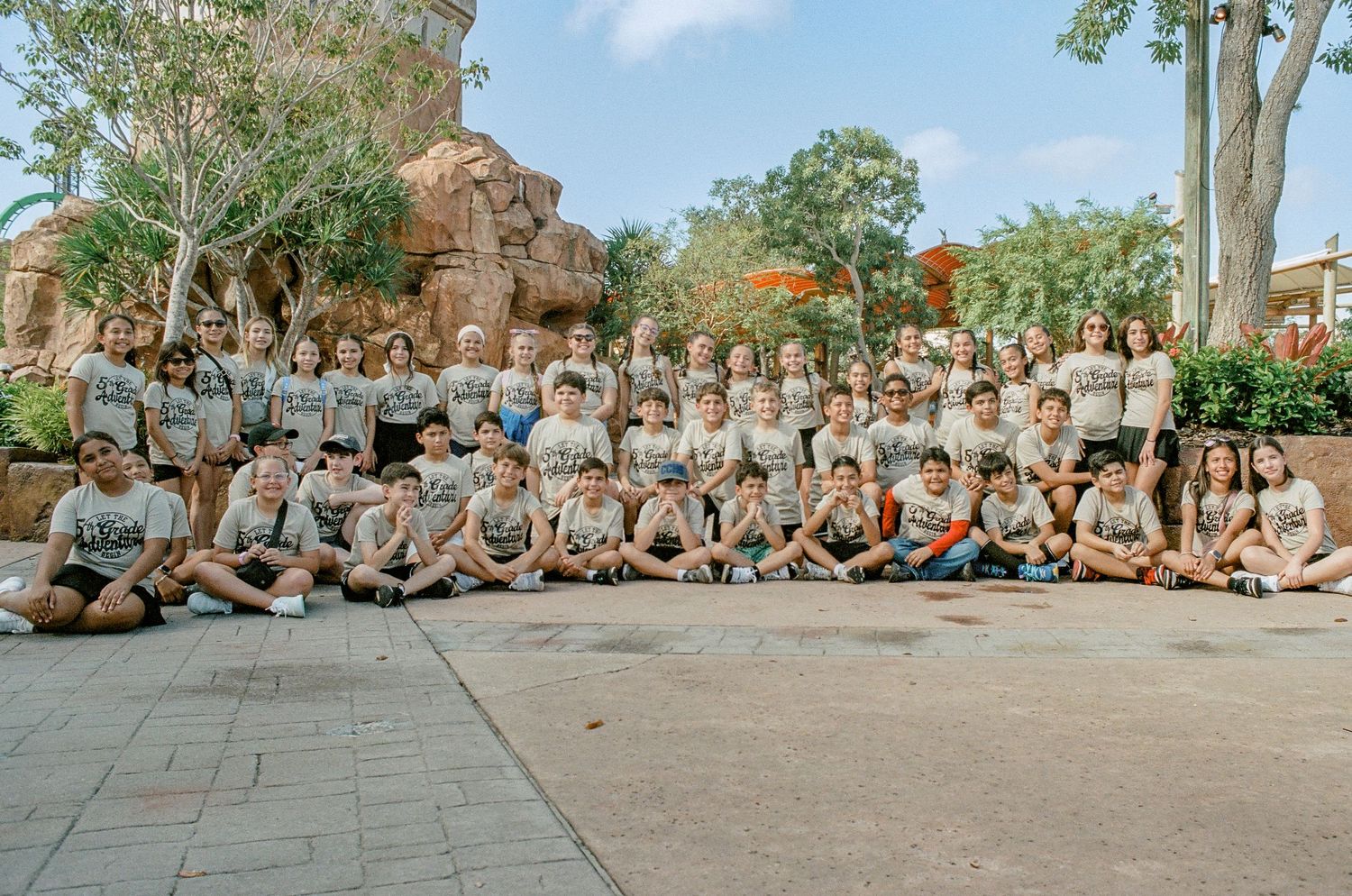 Large group sitting together outdoors in matching gray shirts for a group photo.