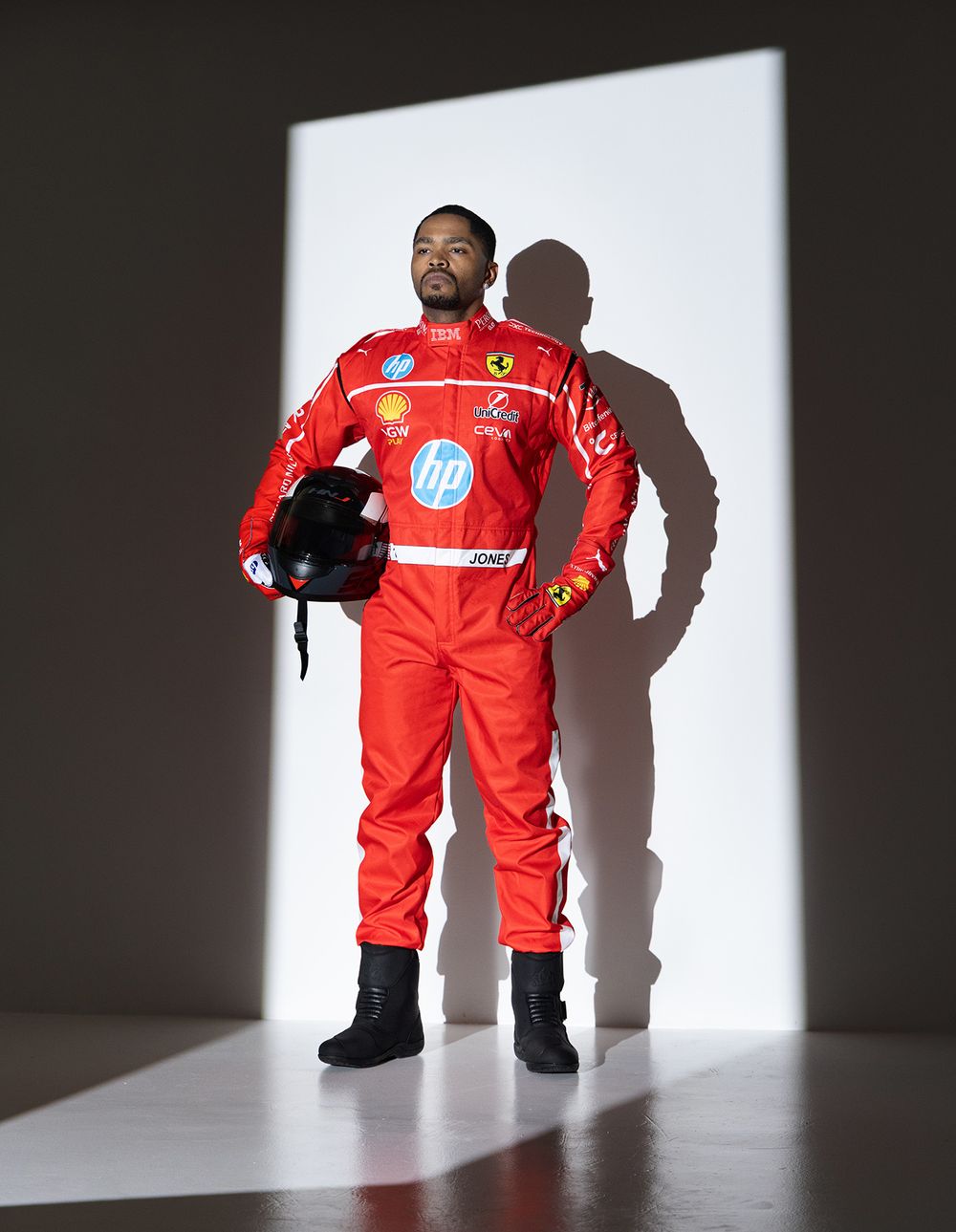 A race car driver in a bright red racing suit stands confidently casting a shadow against a white backdrop.