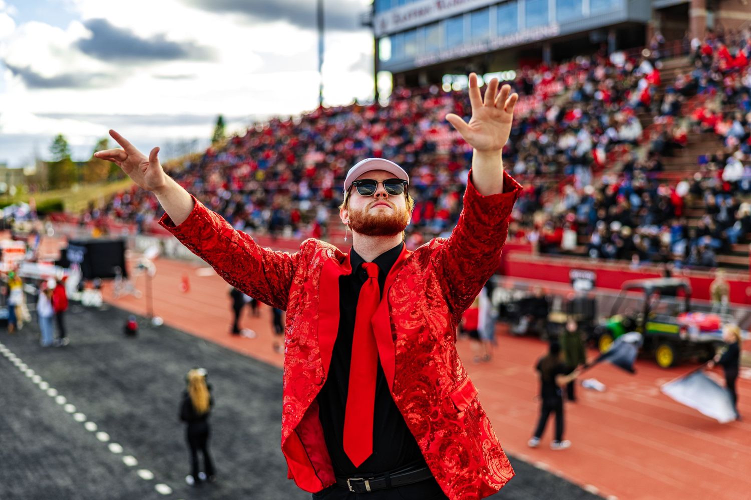 A person in a bright red sequined jacket performs celebratory gestures in a stadium setting during an event.