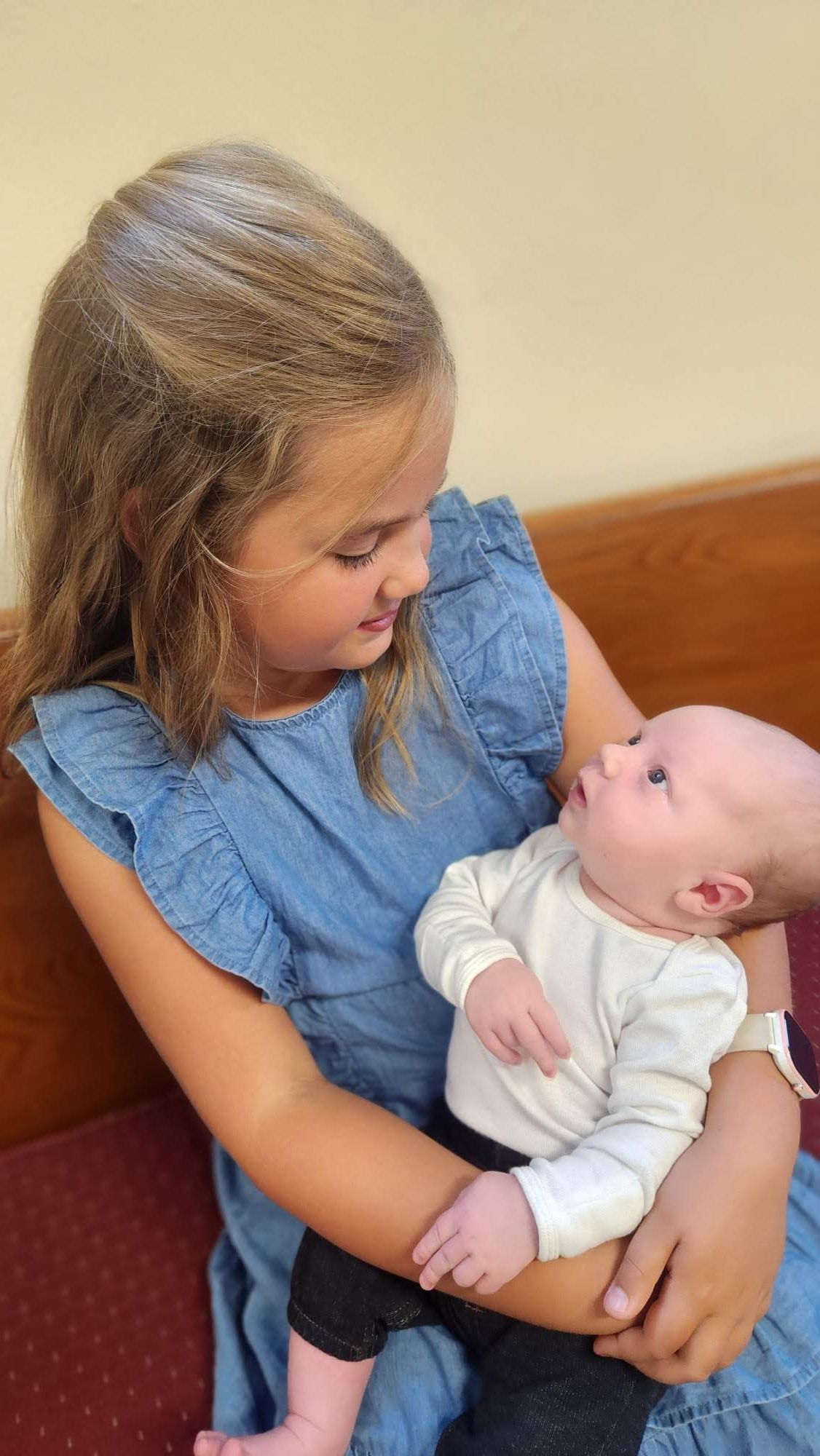 Image of a young girl holding a baby while they both look at each other.