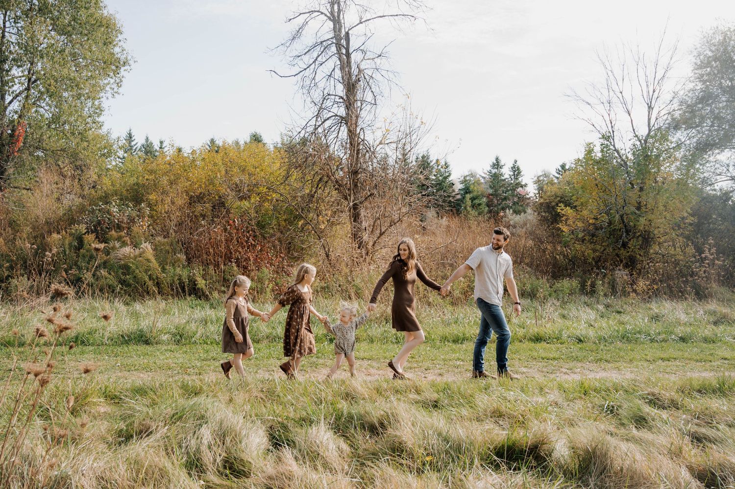 Family jumping and playing together in a grassy field during autumn.