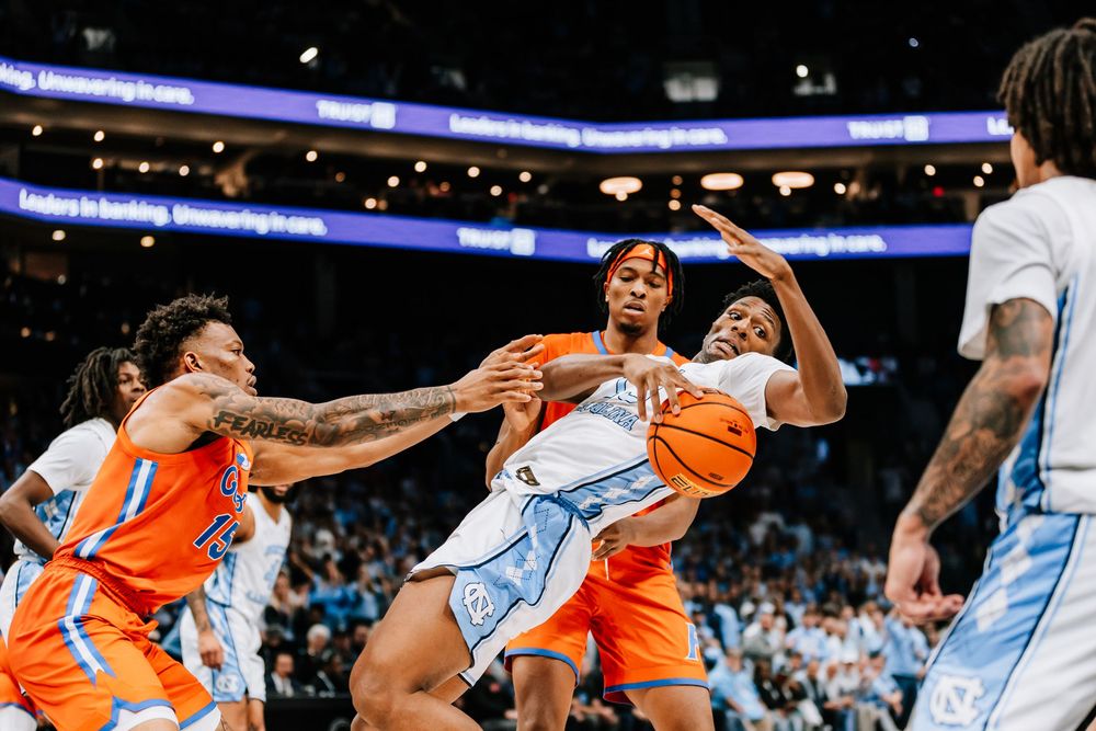 UNC Tar Heels player fights for a rebound against Florida Gators defenders during an intense college basketball game.