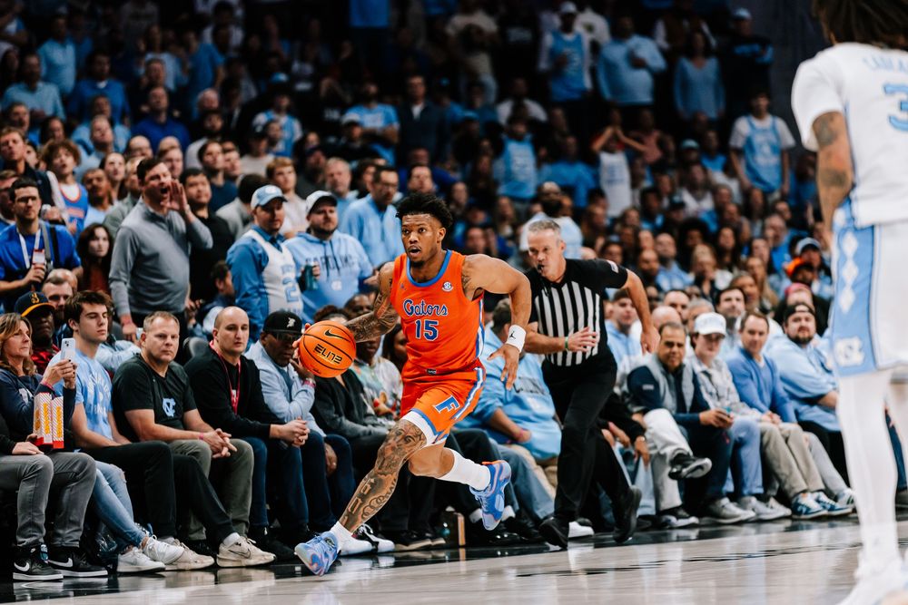 Florida Gators #15 dribbles along the sideline in front of a packed crowd during a college basketball game.