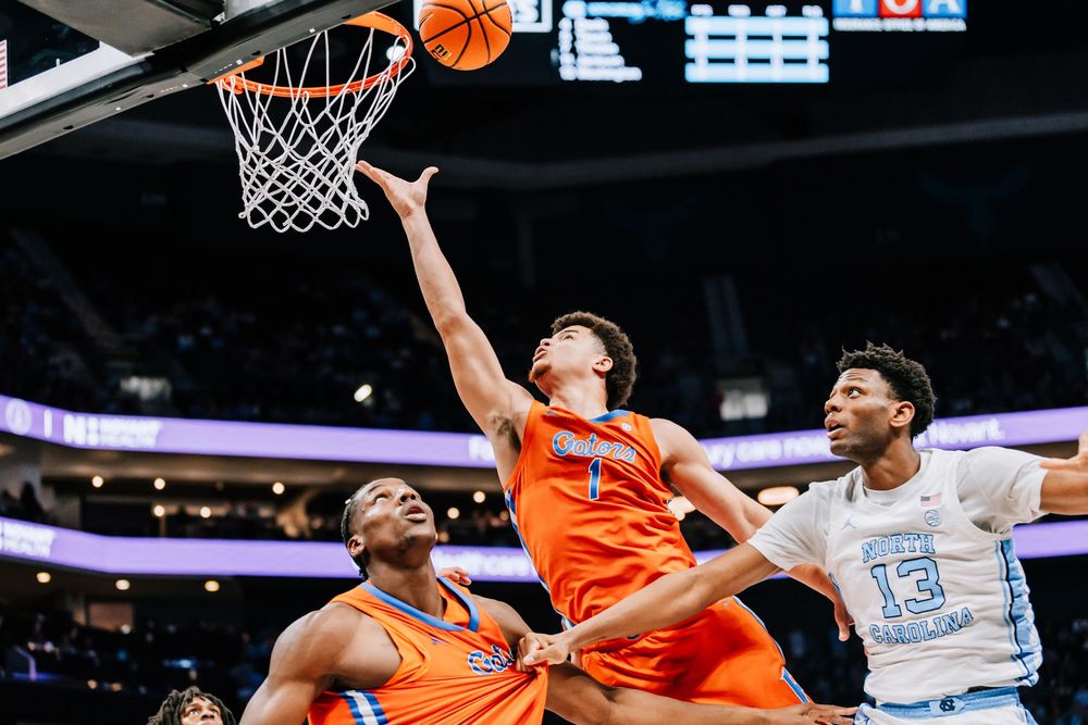 Florida Gators #1 attempts a layup between two North Carolina Tar Heels defenders during a college basketball game.
