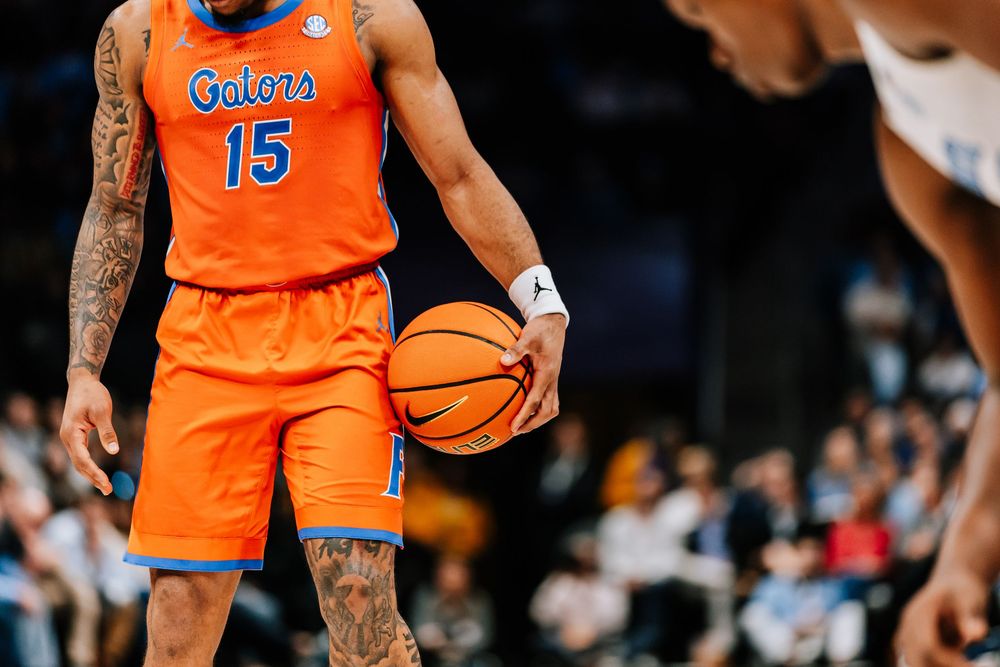 Florida Gators basketball player number 15 dribbles ball in orange uniform with tattoos visible.