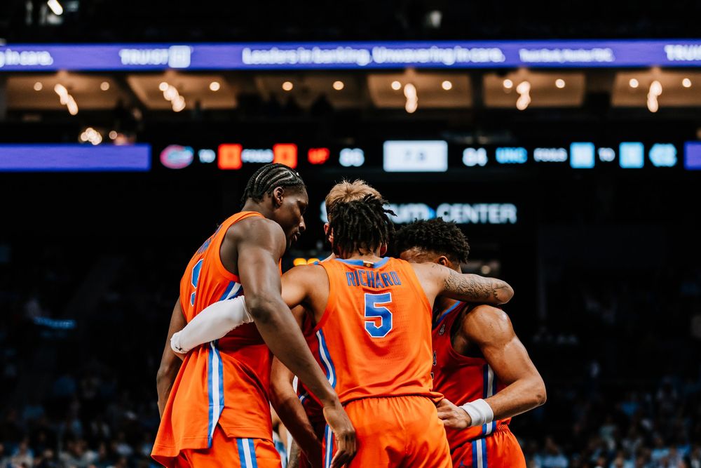 Florida Gators basketball team huddles together in orange uniforms during a college basketball game.