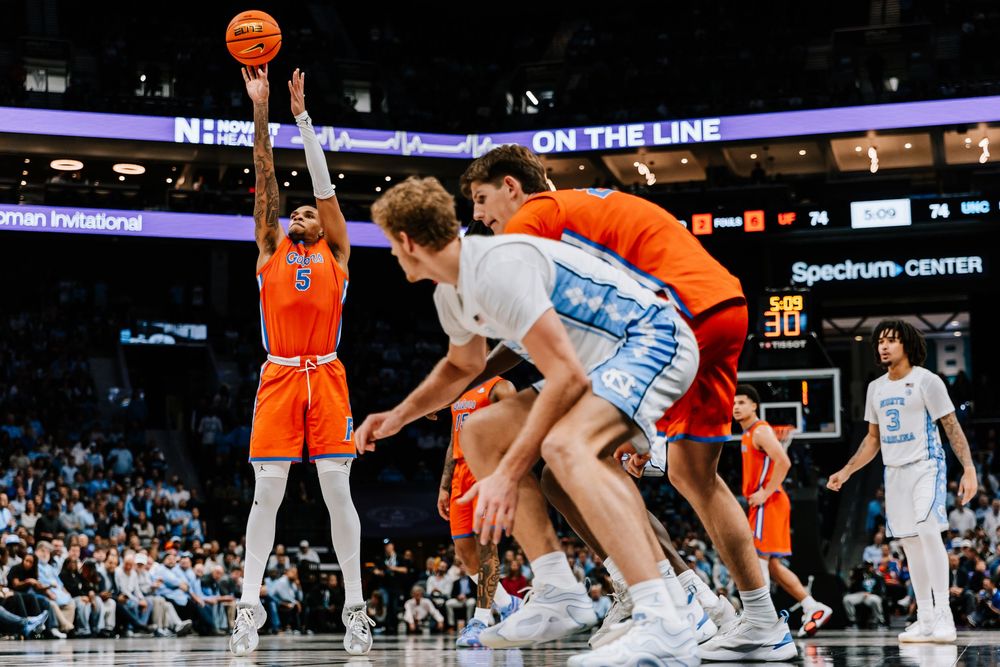 Florida Gators player #5 shoots over UNC Tar Heels defenders during college basketball game.