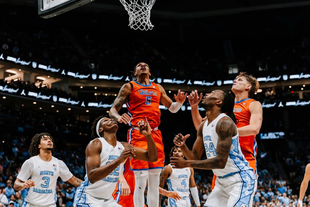Florida Gators player battles UNC Tar Heels defenders for a rebound during college basketball game.