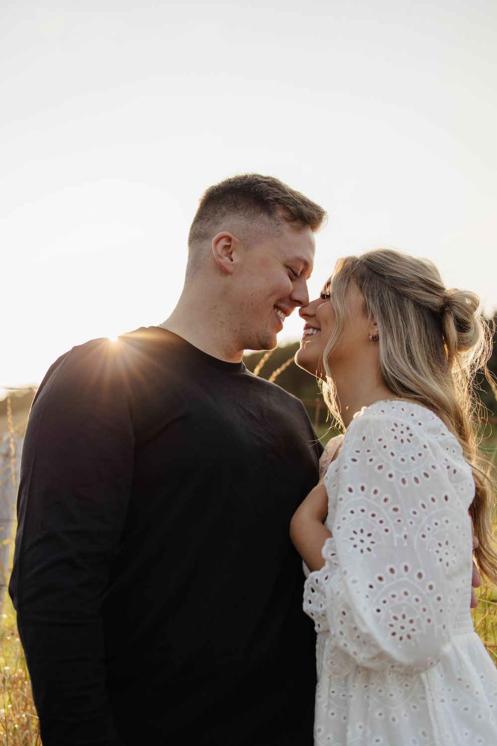Romantic couple laughing together in sunlit field during sunset photoshoot.