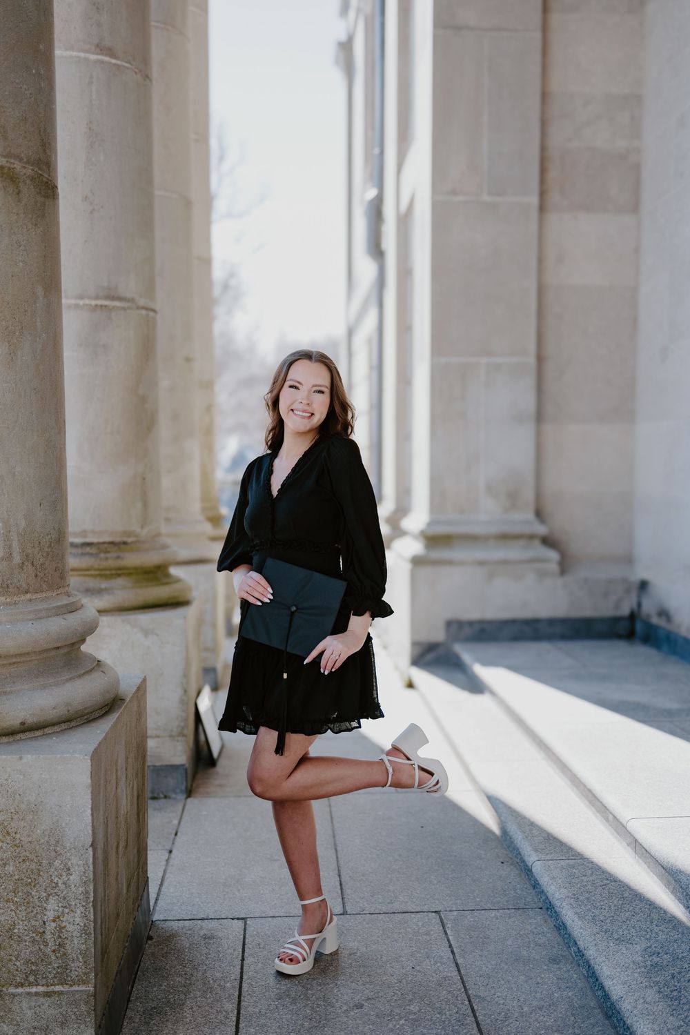 St. John's photographer captures woman in black dress poses confidently between classic stone columns in natural light.